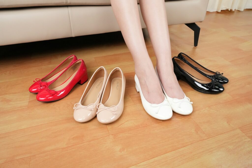 Frau auf einer Couch neben drei Paar Schuhen, Symbolbild zur Frage Ballerinas oder Loafer