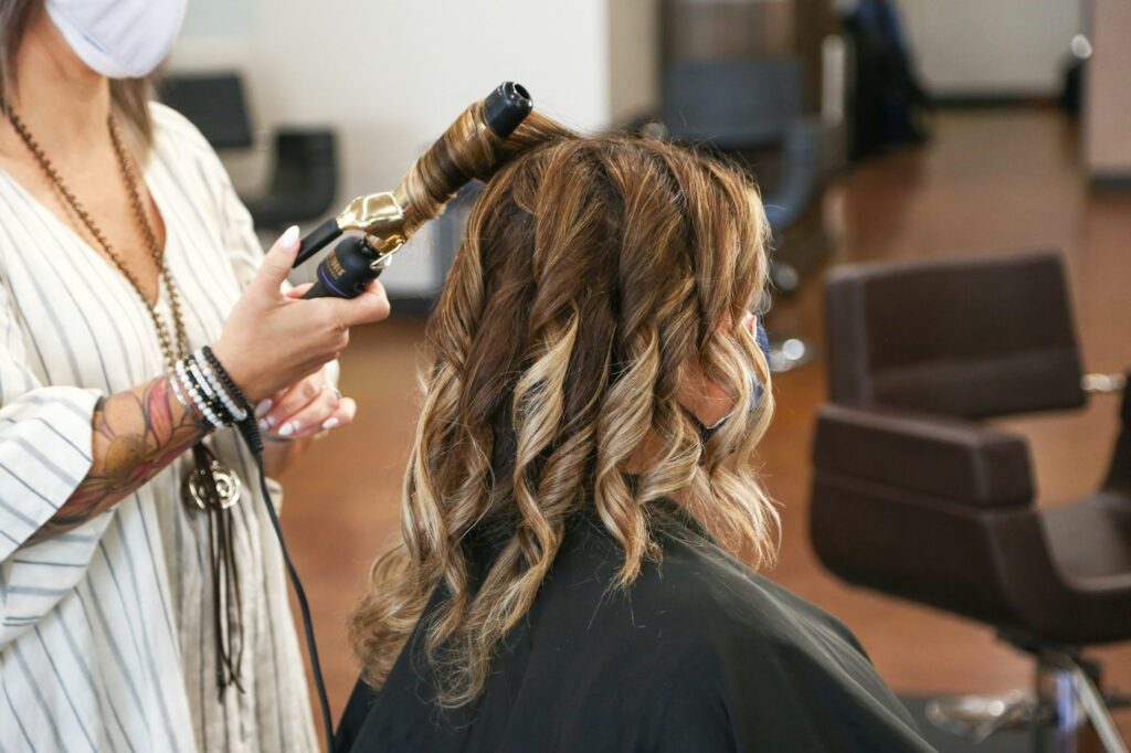 Friseurin stylt im Salon frisch gefärbtes Haar mit einem Lockenstab