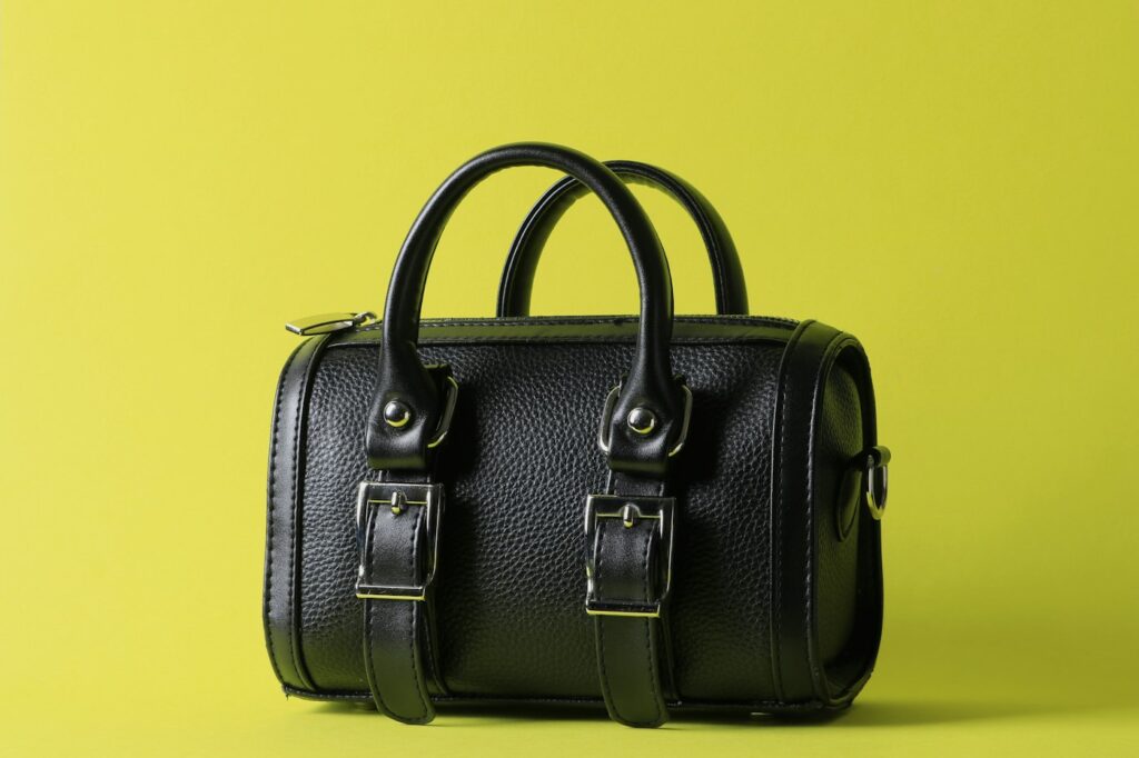 Schwarze Ledertasche im Stil der It-Bags auf gelbem Hintergrund