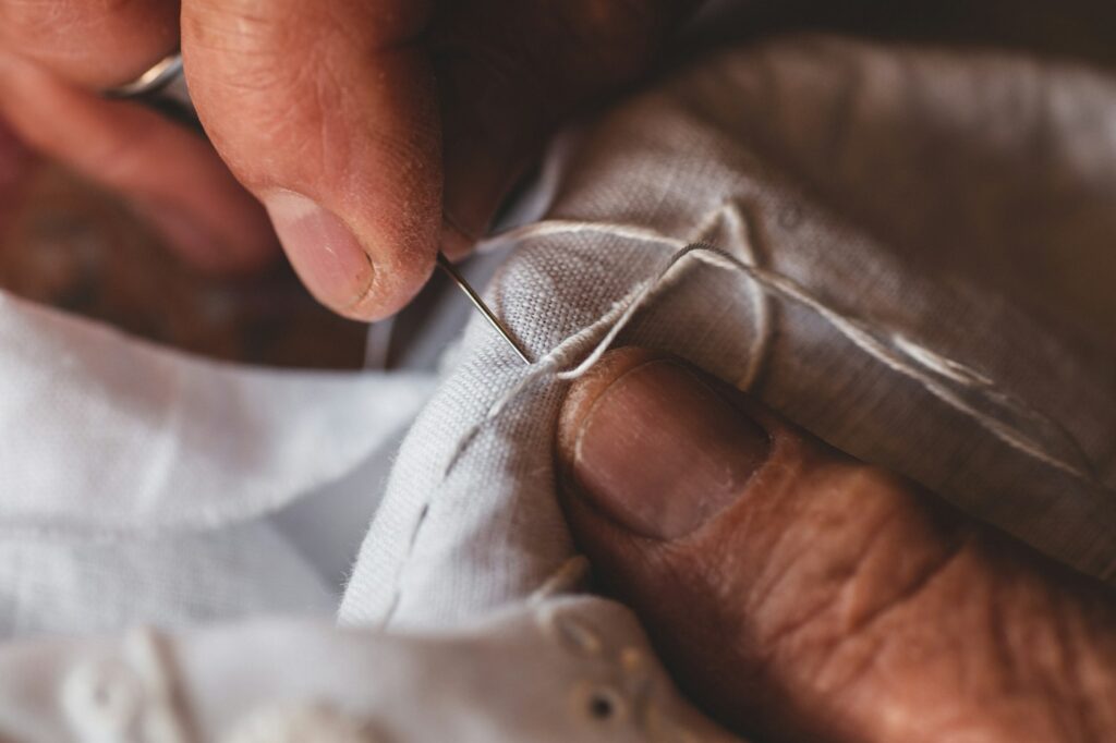 Hände nähen weißen Stoff mit Nadel und Faden, um Kleidung zu reparieren